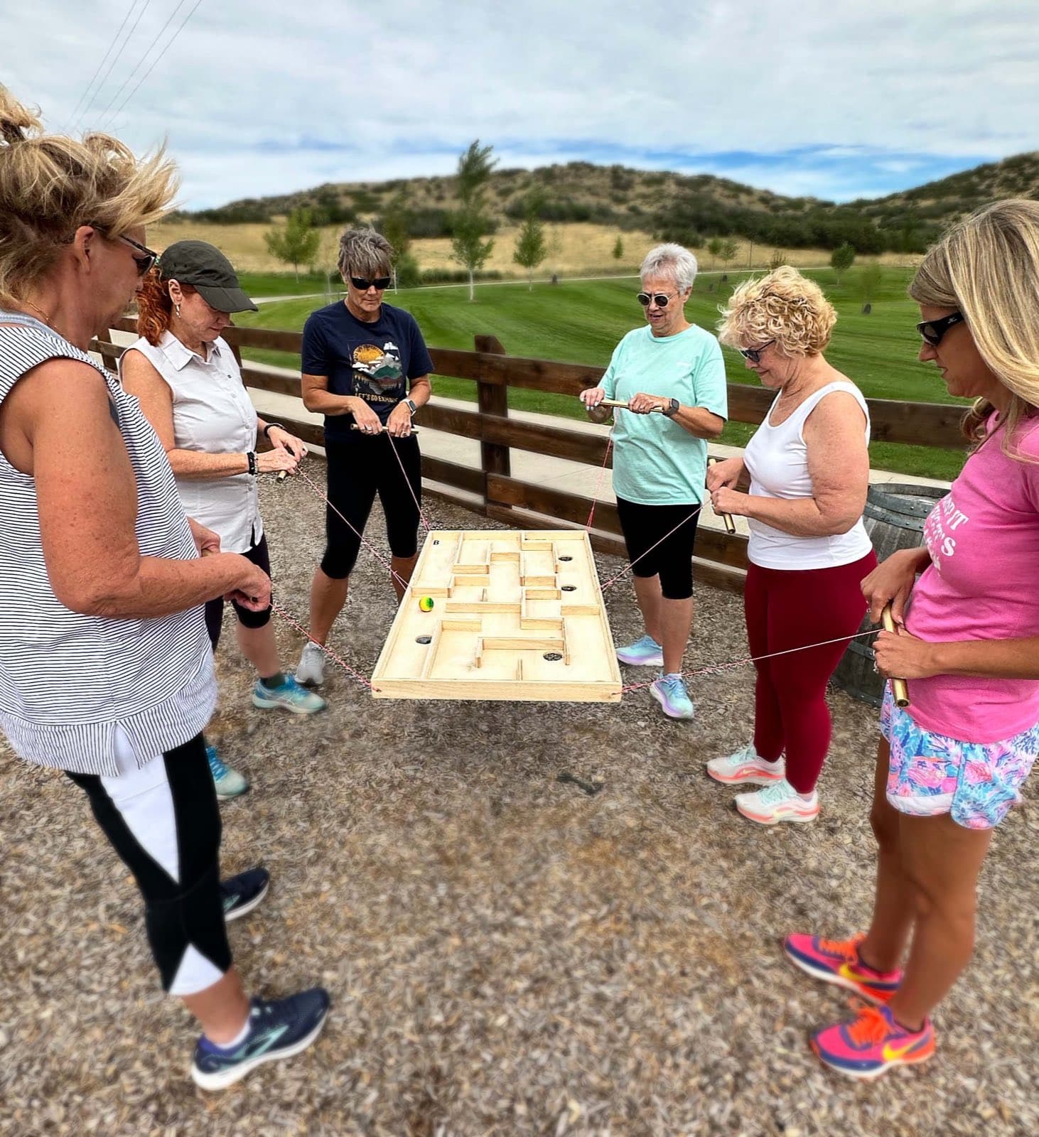 A group guides a ball through a string-suspended maze board during a facilitated team building game at The EDGE